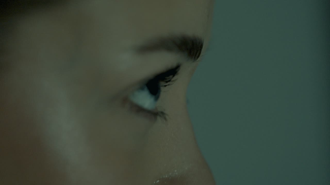 Side profile closeup of a woman intensely focused during indoor cycling, her eyes locked straight ahead. Cinematic lighting highlights her concentration, strength, and calm control mid-workout