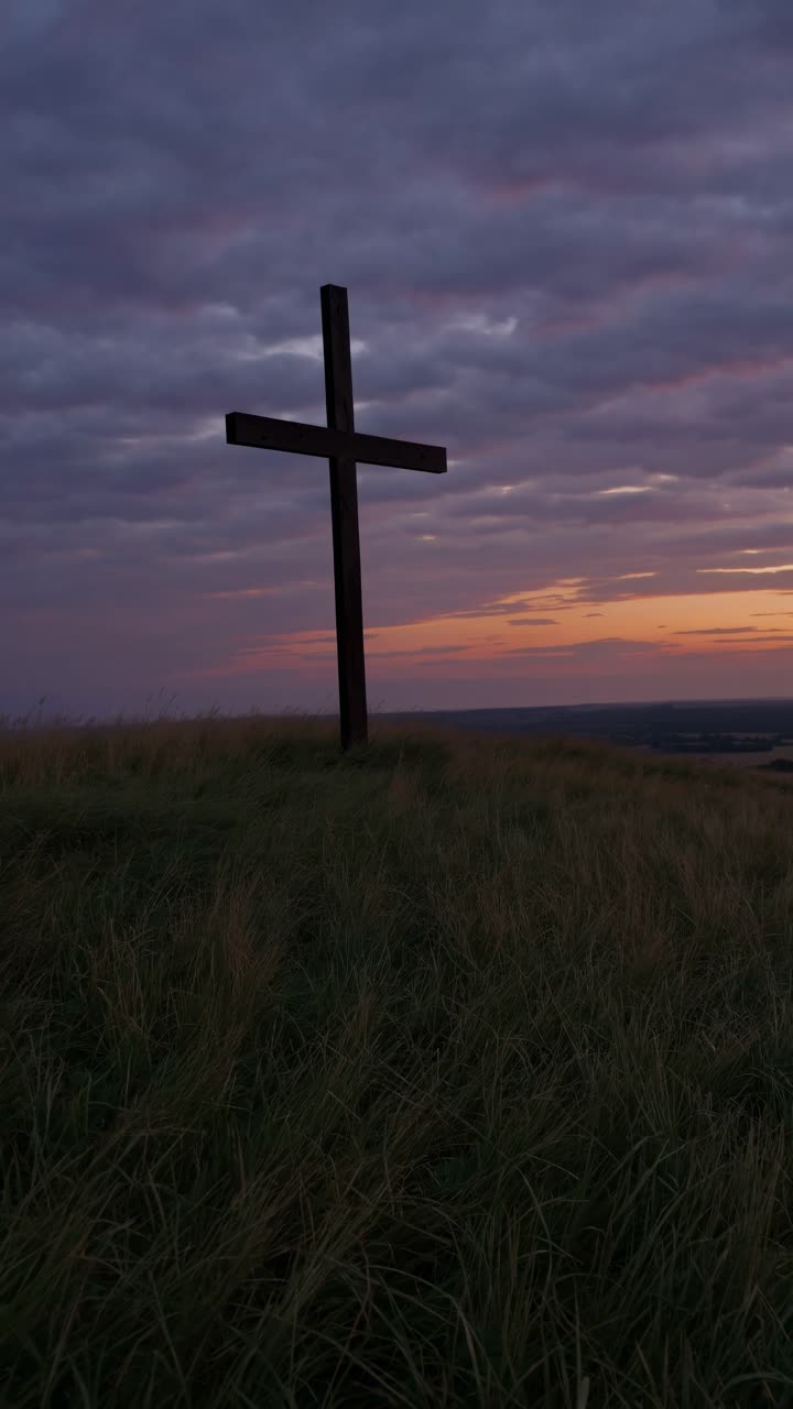 Un fotogramma video sereno di una croce su una collina al tramonto, ripreso da una bassa angolazione.