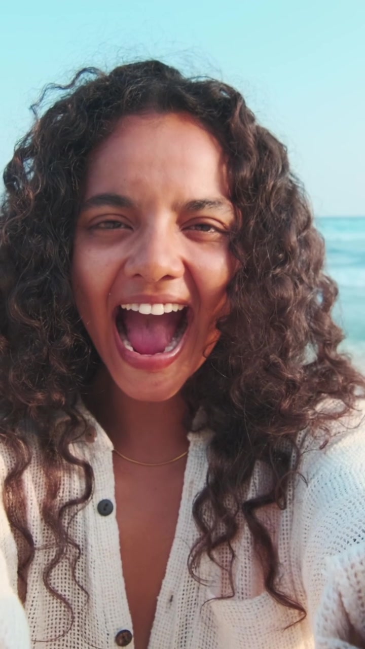 Donna sorridente in piedi sulla spiaggia durante una giornata di sole con il cielo azzurro.