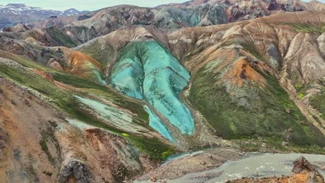 aerial drone fast backward movement at medium altitude, over grænihryggur, the green rock, the river, and the valley in landmannalaugar, iceland, highlighting medium tones of orange and green