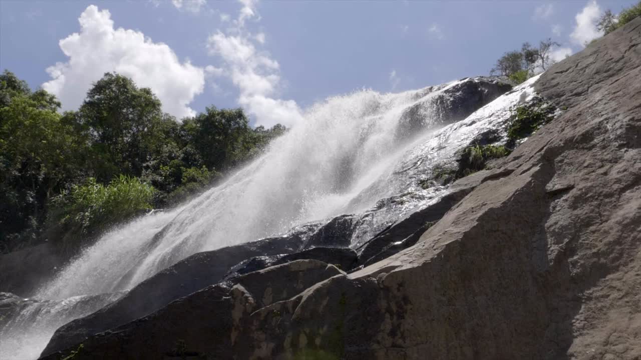 vista de ángulo bajo hasta limpiar la cascada en cascada frente al cielo azul - árboles verdes del bosque