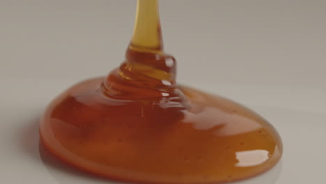 macro studio product shot of natural orange honey pouring on white surface in slow motion