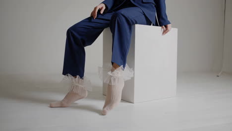 person in blue suit and ruffled socks sitting on white cube