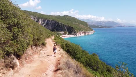 tourist girl walks to beautiful gjipe beach in albania - aerial dolly follow