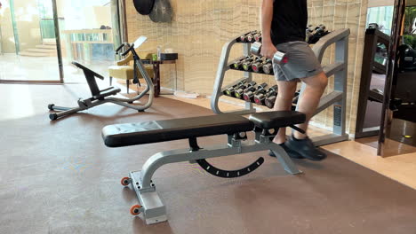 young asian man selecting dumbbells and bench pressing in an upscale, luxurious gym setting