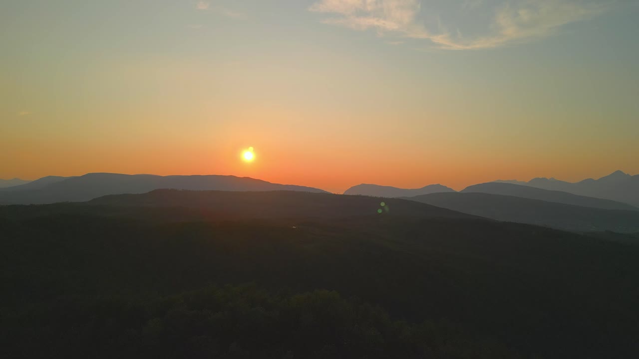A glowing sunset casts warm light over distant mountain ranges, creating a peaceful and colorful evening sky.