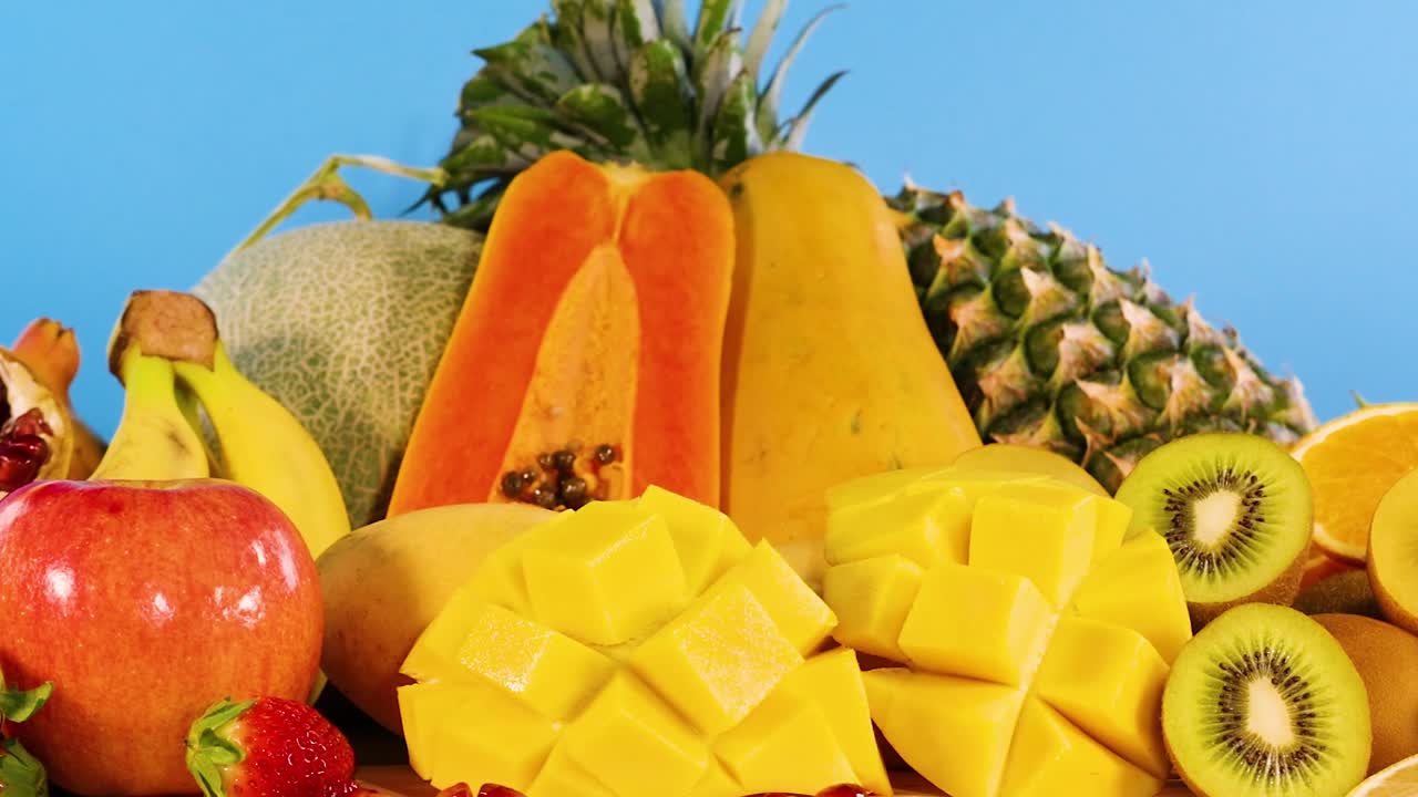 A colorful assortment of tropical fruits including papaya, pineapple, and mango on a vivid blue background.