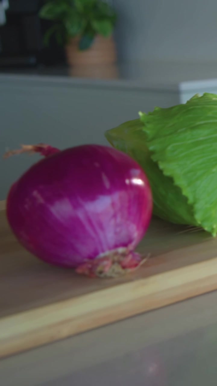 Vertical video: Panning camera showing lettuce wedge on board on counter with onion tomatoes knife