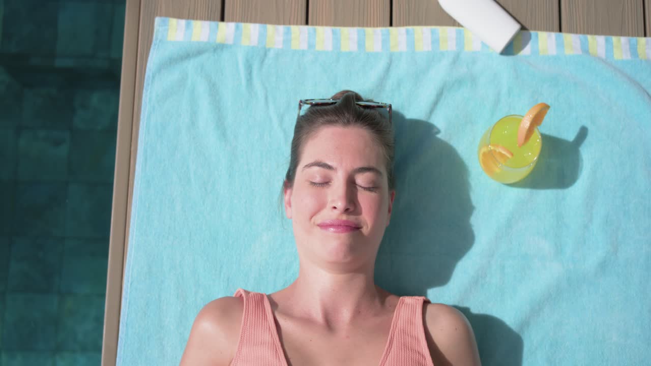 Sunlight causing woman adjusting, lifting shades, closing eyes and stretching on blue towel by pool