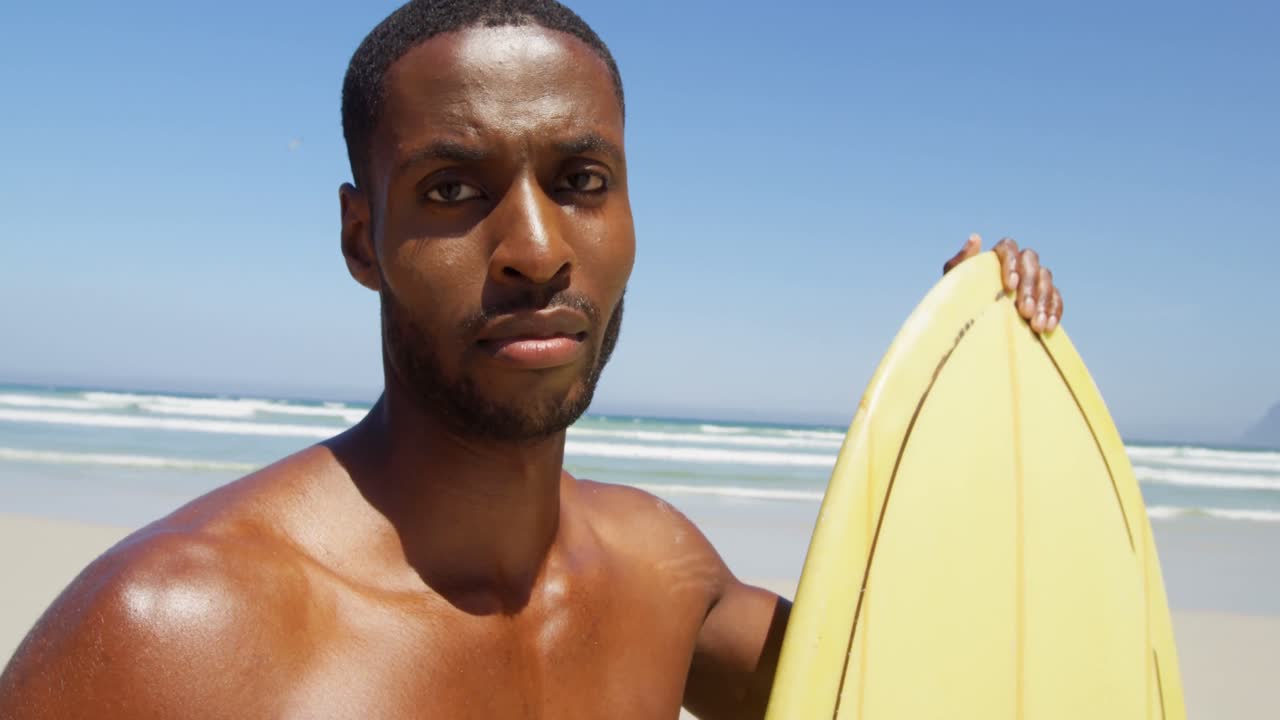 surfista masculino de pie con una tabla de surf en la playa 4k