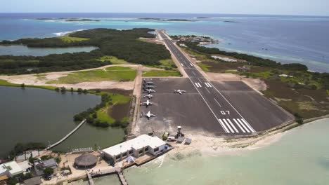 A-small-airstrip-on-gran-roque-with-clear-blue-waters-and-moored-boats,-sunny-day,-aerial-view