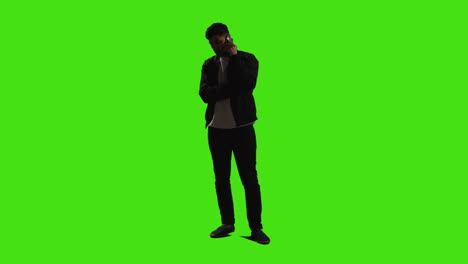 joven hablando en el teléfono móvil de pie contra la pantalla verde con iluminación de baja clave 2