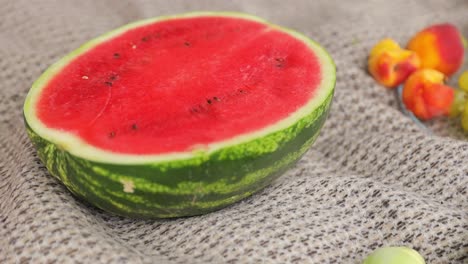 halved watermelon with other fruits on a blanket