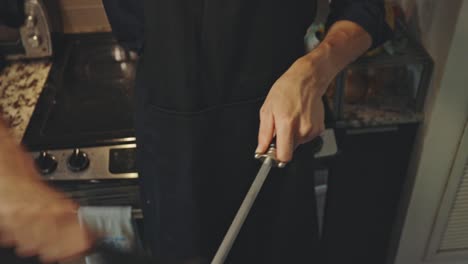 male chef in kitchen sharpening knife with honing rod - close up shot