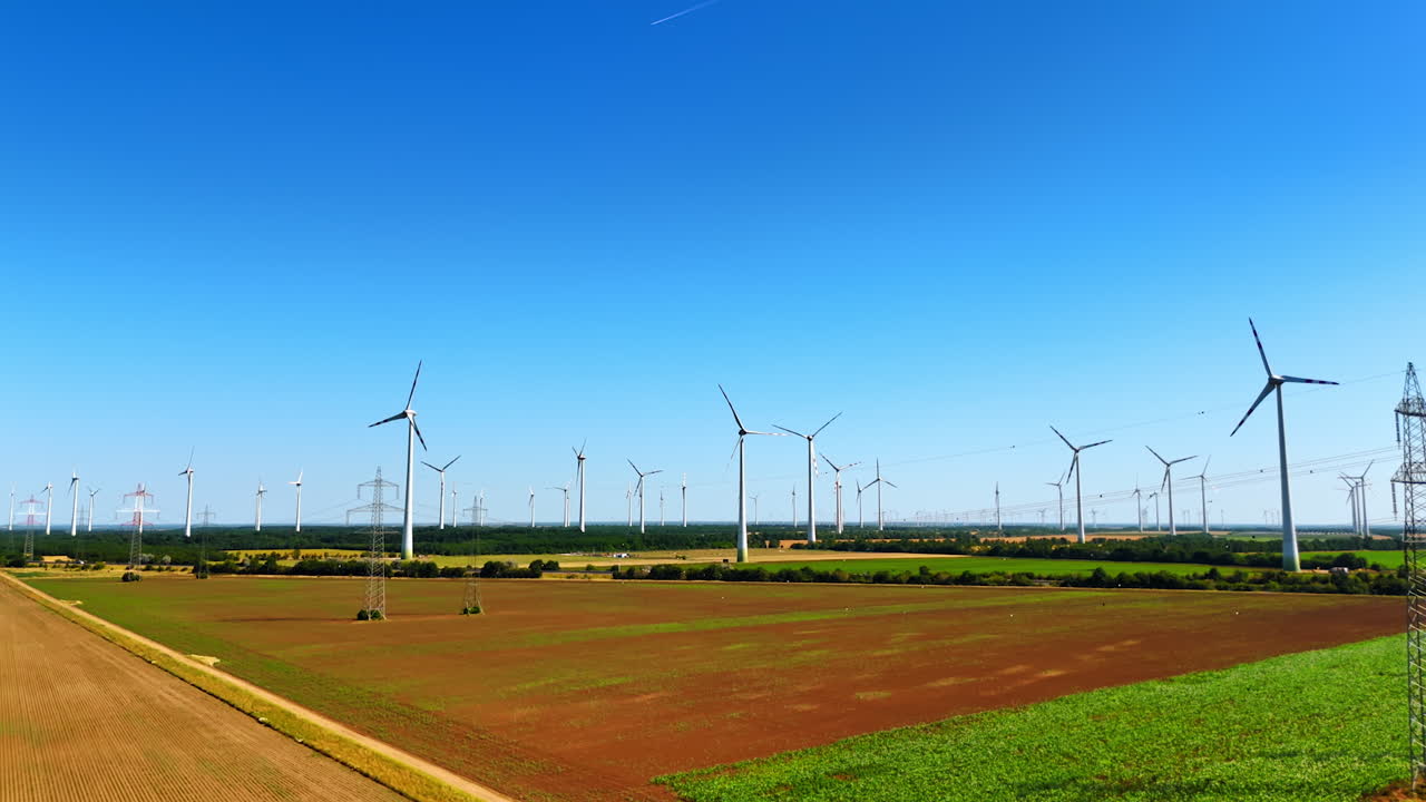 Turbines produce clean power. Vast fields stretch under a clear blue sky, dotted with wind turbines harnessing renewable energy
