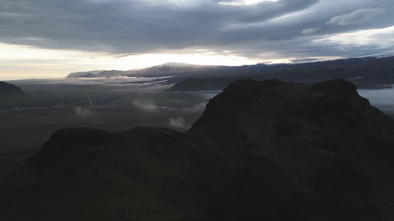 una grúa sin piloto sobre la oscura montaña vik revela la niebla de la meseta de islandia en una brillante puesta de sol.