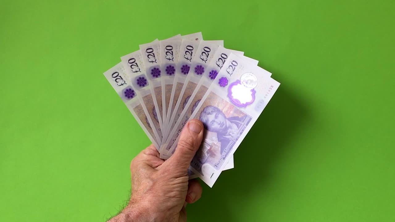 Hand holding British £20 banknotes on green screen