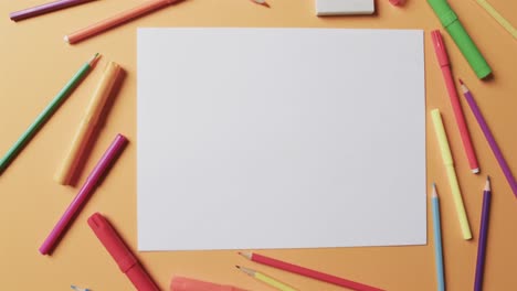 overhead view of blank sheet of paper with school stationery on beige background, in slow motion