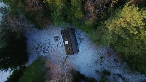 aerial drone top down shot over a small cottage in the middle of woods with thin layer of snow covered on a cold winter day