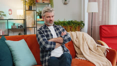 Upset mature man showing thumbs down dislike gesture expressing discontent and disapproval at home