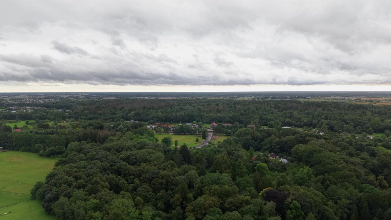 Drone video showcasing expansive green forests, open fields, and rural roads beneath a moody, overcast sky. Wide aerial panorama, natural daylight, no people, serene landscape.