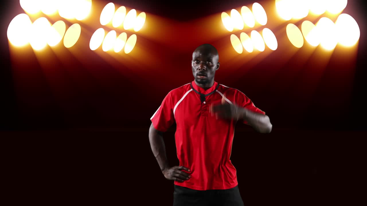 Professional rugby player holding a ball in front of stadium spotlights