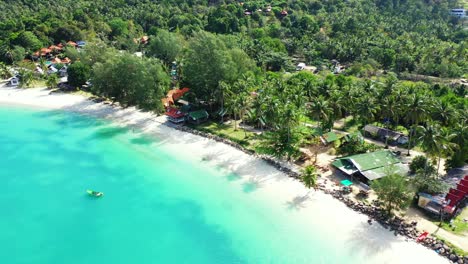 Tropical-island-shoreline-with-palm-trees-and-beach-cabins-near-white-sand-washed-by-calm-turquoise-lagoon-in-Malaysia