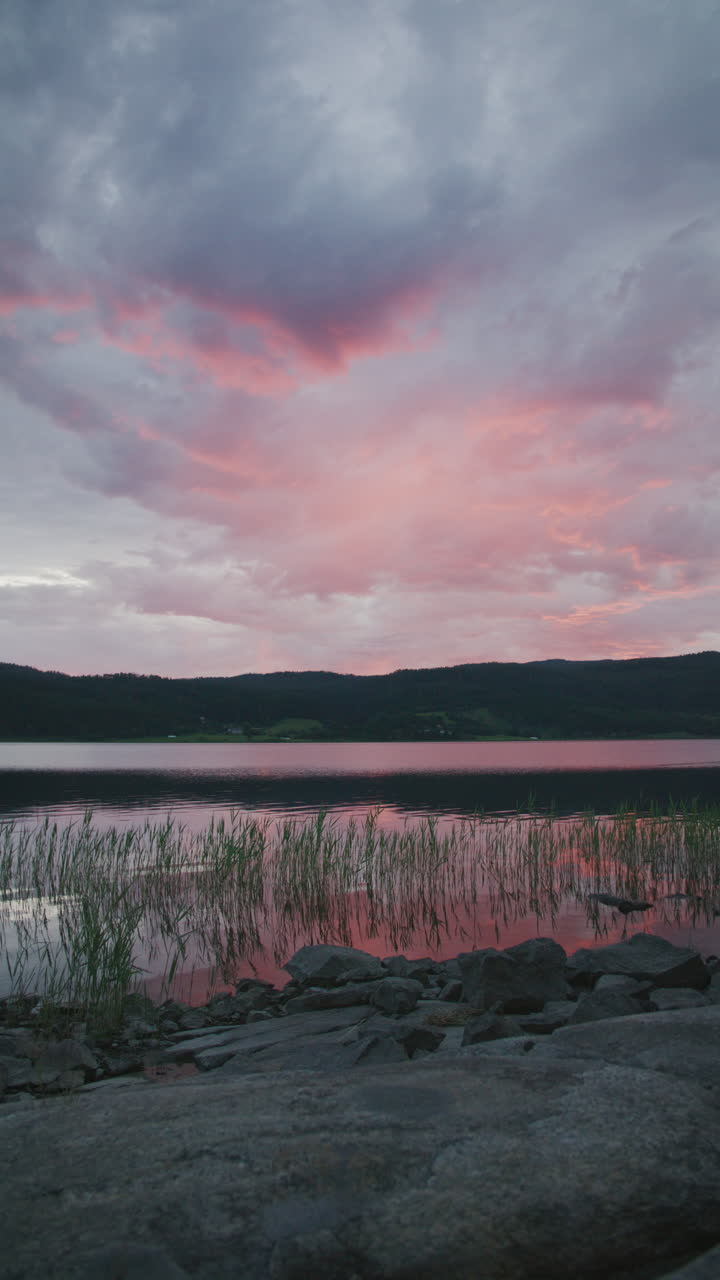 A vertical shot of a lake at sunset, with pink and blue clouds reflecting on water.