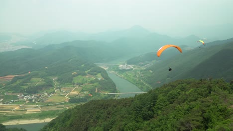 Paraglider-take-off-from-the-mountain-peak-and-paragliding-towards-the-mountain-river-on-cloudy-day-in-South-Korea