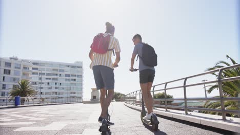 feliz pareja masculina gay diversa usando scooters en el paseo marítimo, cámara lenta