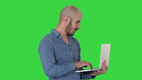 joven empresario de oriente medio, de pie y escribiendo en una computadora portátil cuando la sostiene en sus manos en una pantalla verde, llave de croma