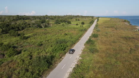 Vista-Aérea-De-Un-Automóvil-Que-Conduce-A-Través-De-La-Carretera-Costera-En-Un-Día-Soleado-En-La-Isla-De-Sumba,-Indonesia