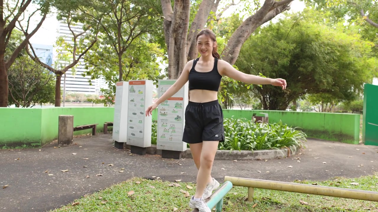 Una mujer tailandesa en forma practica ejercicios de equilibrio en una barra en un gimnasio al aire libre en un parque.