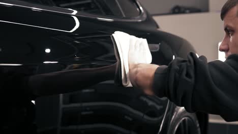 Male-hand-wiping-dust-off-the-surface-of-a-black-car.