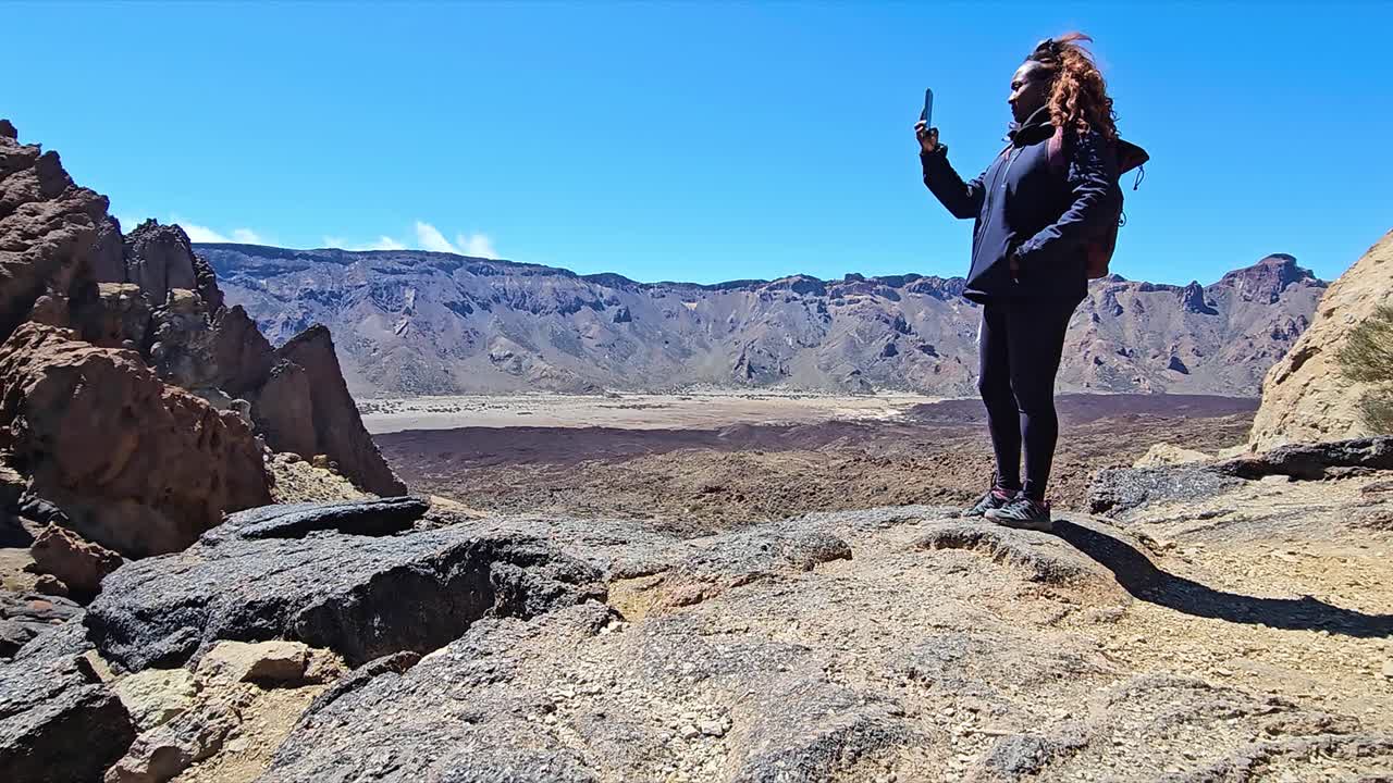 A woman standing on a rock, taking a photo at Roques de Garcia, Spain