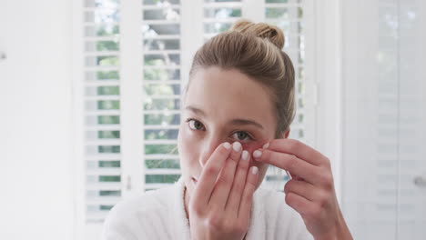 mujer biracial aplicando parches debajo de los ojos en el baño, cámara lenta