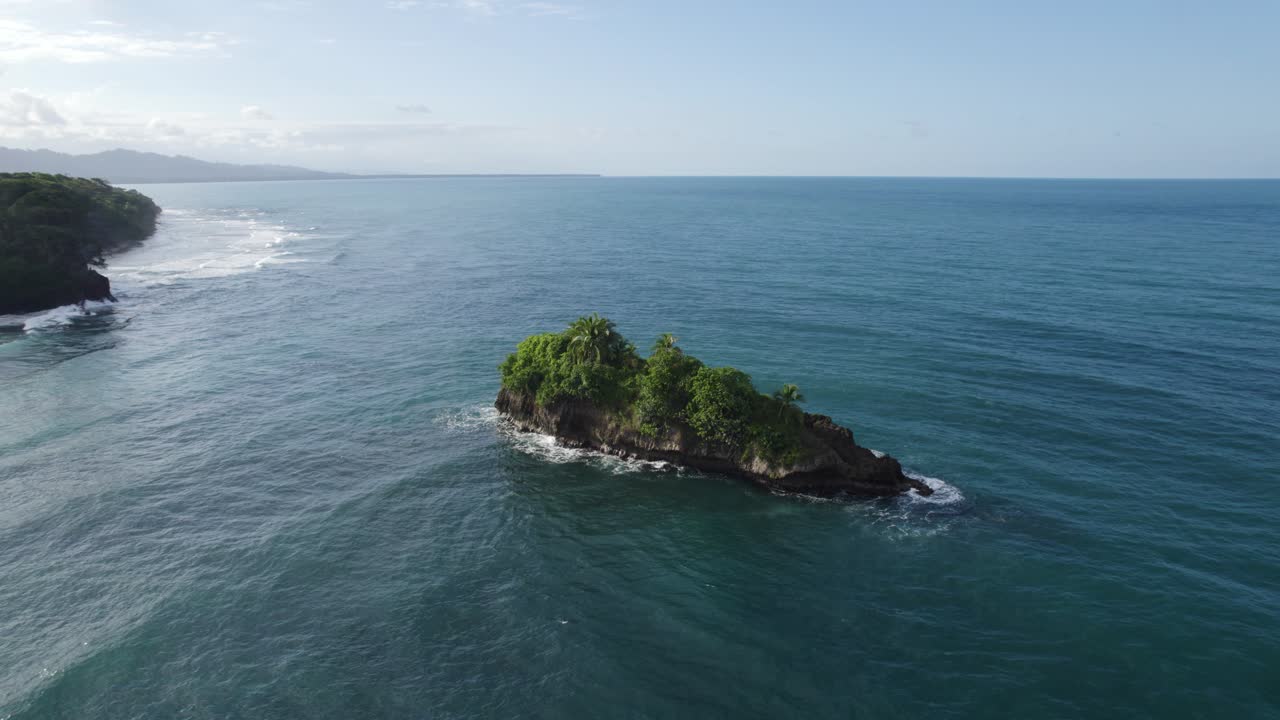 Small rocky island with lush greenery surrounded by blue ocean waters on a sunny day at Puerto Viejo Beach