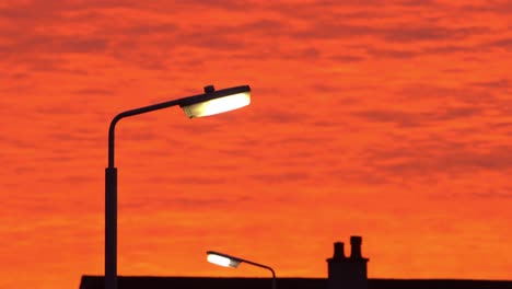 incredible orange red sky at sunset and silhouette of lit street lamps