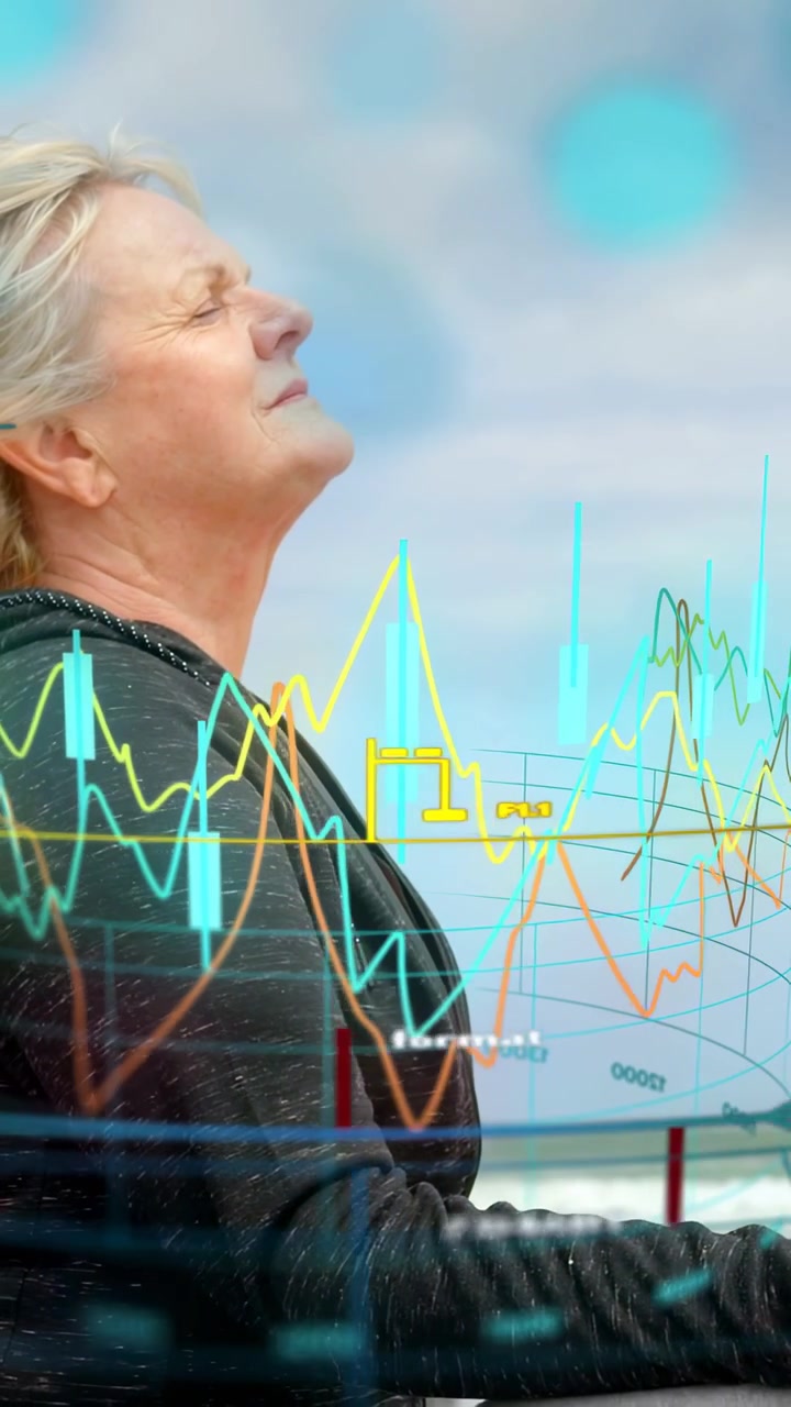 Vertical video: Senior taking breath holding arms to view health graphs flowing before her at coast
