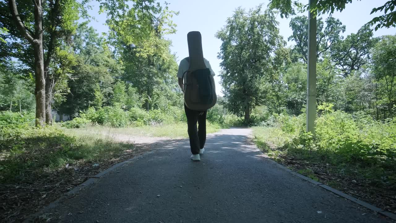 숲 근처의 거리에서 기타를 들고 는 젊은 남자