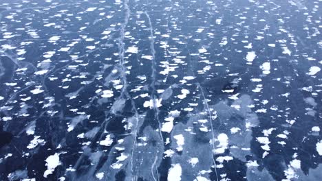 looking down at frozen ice from above and tilting up to reveal snow covered rocky mountains, aerial