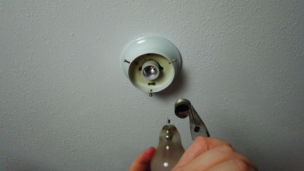 quitando la parte rota de una bombilla con un par de alicates y mirando la bombilla rota