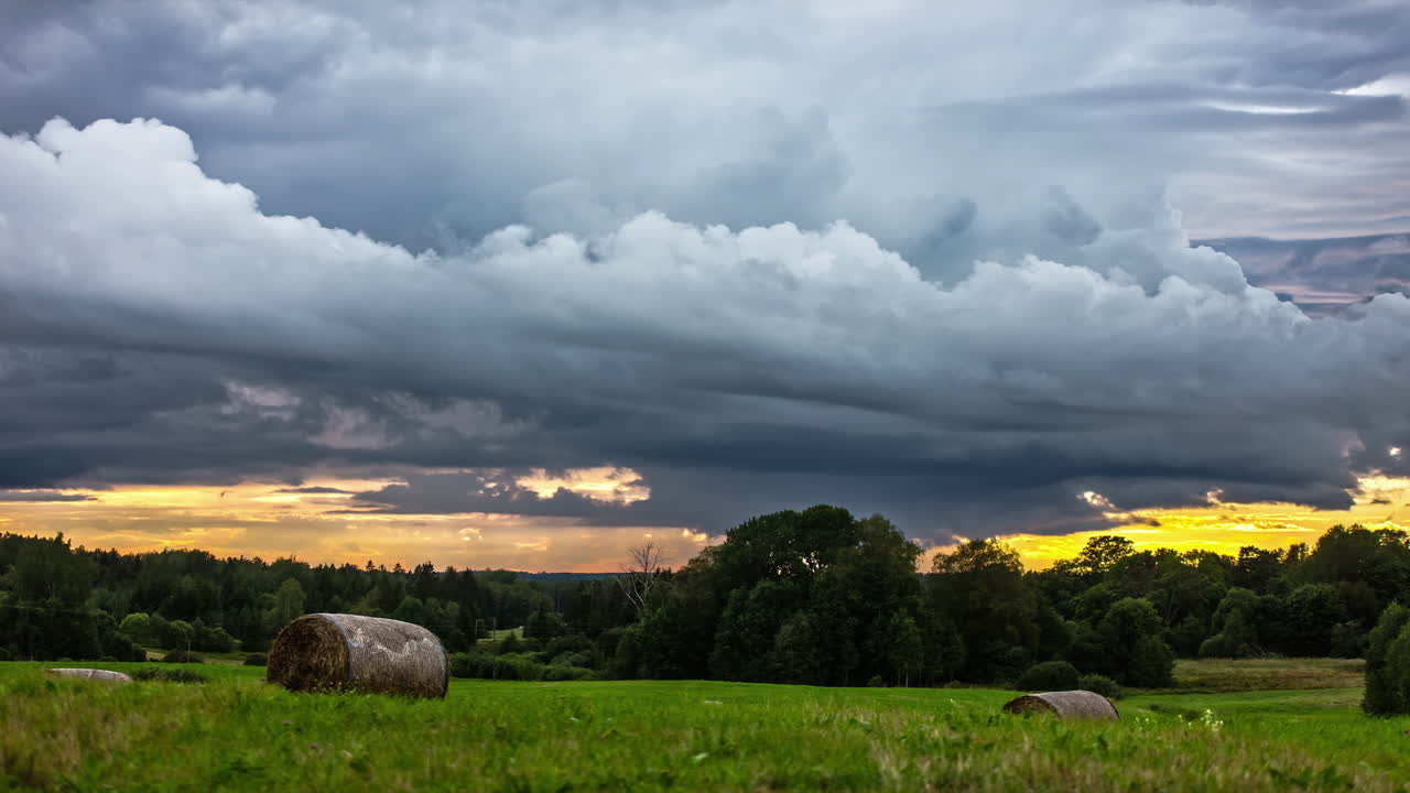 Dunkle Wolken ziehen über einem Ackerfeld, während gelbes Sonnenlicht am Horizont verschwindet – Zeitrafferaufnahme