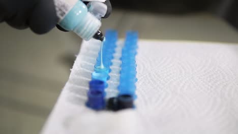 Close-up-shot-of-tattoo-master-dropping-colorful-ink-into-the-containers.-Professional-tattoo-master-filling-the-cups-with-ink-for-working-process.-Slow-motion