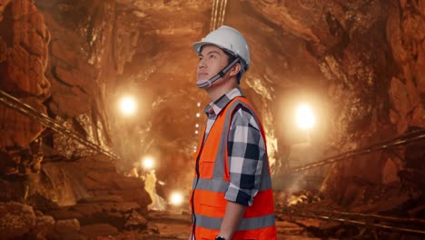 side view of asian male engineer with safety helmet looking around while standing in underground mine tunnel