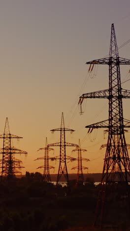 high-voltage power towers. the dark silhouette of towers in the rays of the beautiful evening sun. electric pylons at dusk. global warming. vertical video