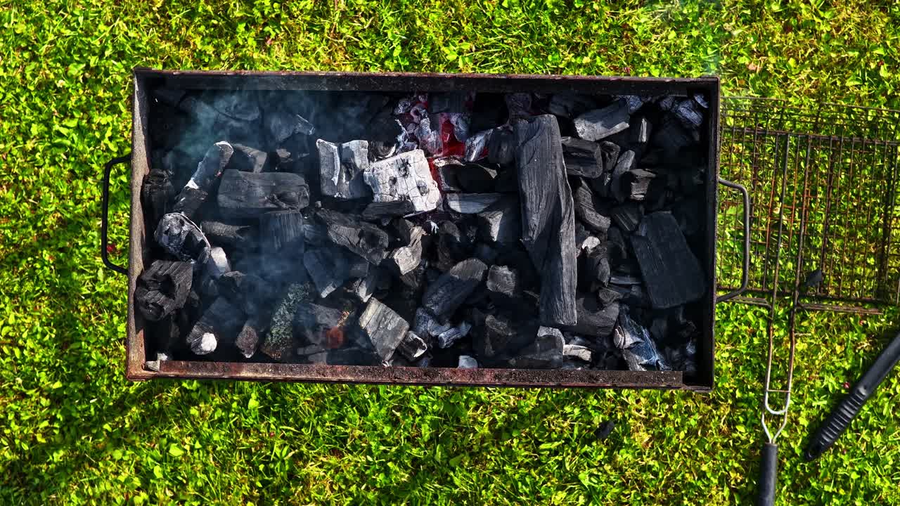 Top shot of barbeque grill with dark burning charcoal pieces at a field