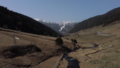 Stream-flowing-through-Andorra-valley-during-summer-season-on-sunny-day-with-snowy-mountains-in-background,-Pyrenees-in-Spain