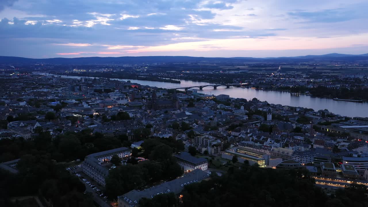 tiro de dron de empuje bajo de mainz en la noche de la hora mágica del centro de la ciudad con la catedral y el agua oscura del río rin en el fondo que muestra un cielo colorido
