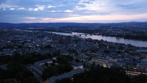 low push in drone shot of mainz at magic hour night of the city center with with the cathedral and the dark rhine river water in the background showing a colorful sky